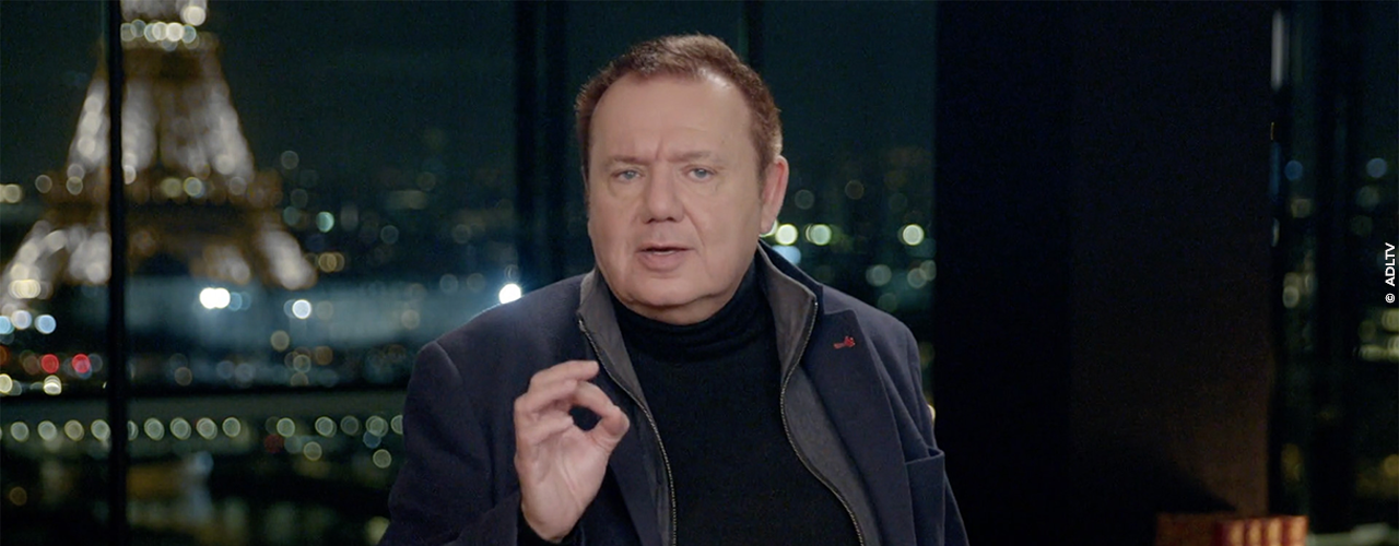 Christophe Bourseiller présentateur de la série devant une fenêtre vue sur la Tour Eiffel