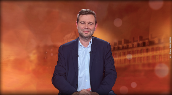 journaliste assis à table devant un décor orangé
