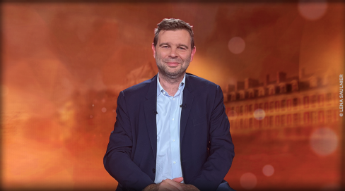 journaliste assis à table devant un décor orangé